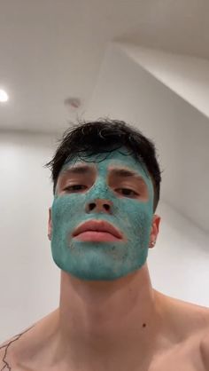 a man with blue facial mask on his face looking at the camera while standing in front of a mirror