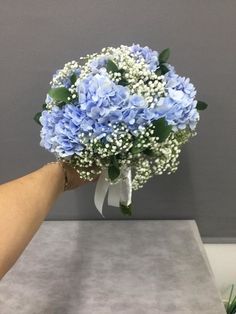 a bouquet of blue flowers being held by a person's hand on a table