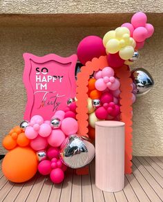 there is a pink sign and balloons on the floor next to each other with an orange balloon