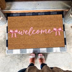 a welcome mat with pink ribbon on the floor next to someone's feet wearing sandals