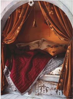 the bed is covered with a red blanket and pillows in an arch over it's headboard