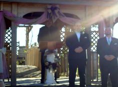 two men in tuxedos are standing under a gazebo at a wedding ceremony