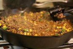 corn and ground beef cooking in a skillet on the stove top with tongs