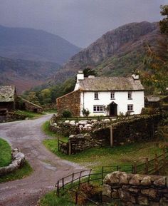 a white house sitting on the side of a road next to a lush green hillside