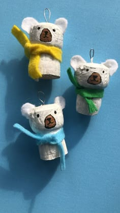 three small stuffed animals are hanging from clothes pins on a blue surface, one is wearing a scarf and the other has a banana in it's mouth