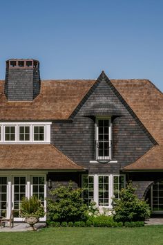 a large brown house with white trim on the windows and shingled roof, surrounded by lush green grass