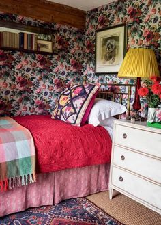 a bedroom with floral wallpaper and red bedspread on the bed, two nightstands next to each other