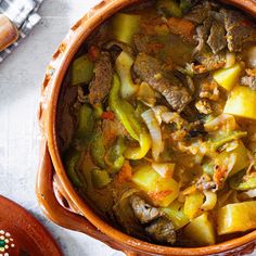 a pot filled with meat and vegetables sitting on top of a table next to a spoon