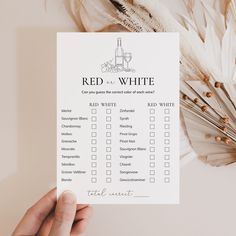 a person holding up a red and white checklist on top of a table next to feathers