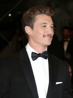 a man in a tuxedo smiles as he walks down the red carpet at an event