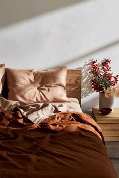 an unmade bed with two vases and flowers on the nightstand next to it