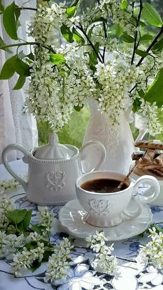 a table topped with white vases filled with flowers next to a cup of coffee