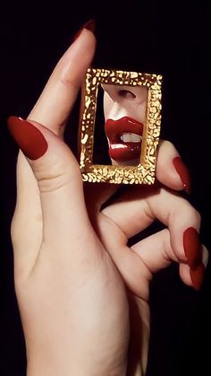 a woman with red nails holding up a golden square shaped object in her hands,