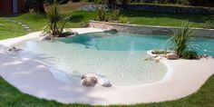 an empty pool in the middle of a yard with grass and rocks around it, next to a house