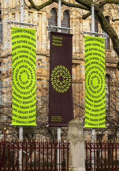 three green banners with words on them hanging from poles in front of a large building