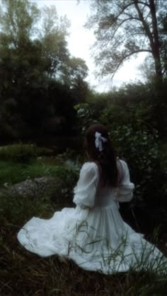 a woman in a white dress is sitting on the grass and looking at something behind her