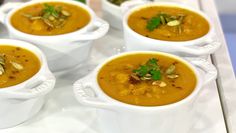 four white bowls filled with soup and garnished with nuts on the top, sitting on a tray