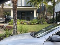 a car is parked in front of a house with palm trees and landscaping around it