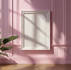 a pink wall with a white frame hanging on it and a plant in the corner