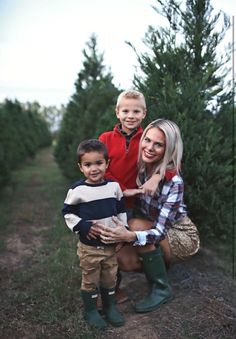 a woman and two boys standing in front of a row of christmas tree's