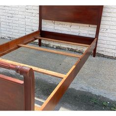 a wooden bed frame sitting on top of a sidewalk next to a white brick wall