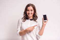 a woman holding up a smart phone in one hand and pointing at it with the other