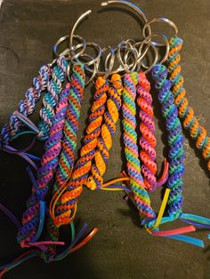 several multicolored bracelets with metal rings on a black surface and one is being held in the other hand