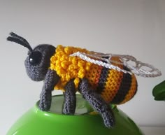 a crocheted bee sitting on top of a green vase