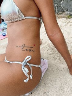 a woman with a tattoo on her stomach sitting in the sand and looking at something