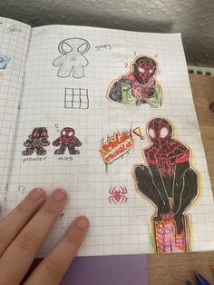 a hand is holding an open notebook with drawings on it and various stickers in the pages