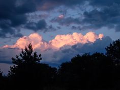 the clouds are pink and blue as the sun sets in the sky behind them on a cloudy day