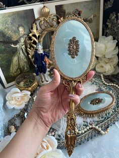 a person holding up a mirror in front of some pictures on a table with flowers and figurines