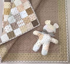 a teddy bear laying on top of a blanket next to a quilted piece of cloth