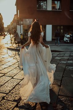 a woman is walking down the street wearing a white dress and holding her hands behind her back