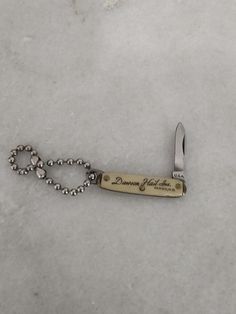 a swiss army knife with a beaded chain attached to it's blade, on a white surface