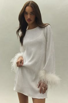 a woman in a white sweater dress with feathers on her arms and legs, posing for the camera