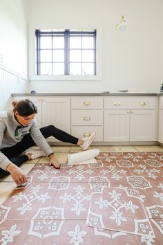 a woman is laying on the floor in her kitchen and painting it with white paint