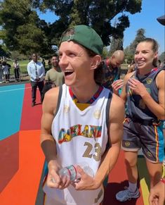 a man in a basketball uniform is laughing and holding a water bottle while people watch from the sidelines