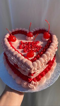 a heart shaped cake with cherries on top is being held by a woman's hand