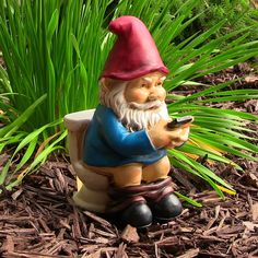 a garden gnome sitting on the ground with a cell phone in his hand and grass behind him