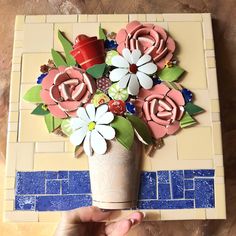 a hand holding a paper flower arrangement on top of a mosaic tile flooring area