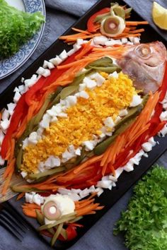 a platter filled with fish and vegetables on top of a blue table cloth next to silverware