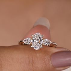 a woman's hand holding an engagement ring with three pear shaped diamonds on it