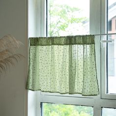 a window with a green curtain hanging from it's side next to a potted plant