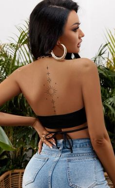 the back of a woman with tattoos on her upper and lower body, standing in front of potted plants