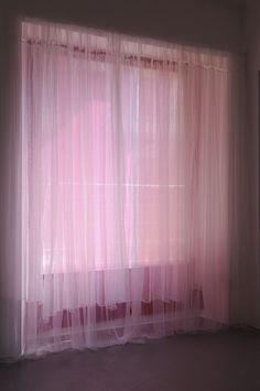 a pink curtain is hanging in front of a window with the light coming through it