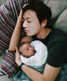 a woman holding a baby in her arms while laying on top of a couch next to pillows