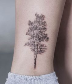 a small tree tattoo on the back of a woman's right leg, with trees growing from it