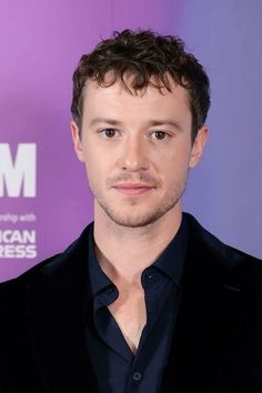 a close up of a person wearing a suit and black shirt with a purple background