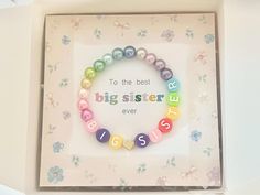 a colorful bracelet with the words sister written on it in front of a flowered background